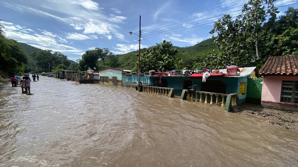Pessoas ficam do lado de fora de suas casas inundadas depois que um rio encheu devido s fortes chuvas aps a passagem do furaco Beryl na Venezuela (Foto: VICTOR GONZALEZ / AFP
)
