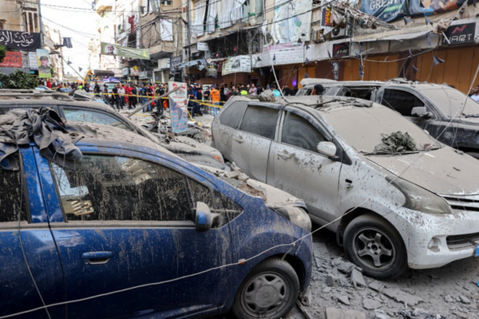 Pessoas atrs de uma rea fechada em uma rua sob um prdio residencial cujos dois ltimos andares foram atingidos por um ataque israelense (Crditos: ANWAR AMRO / AFP)