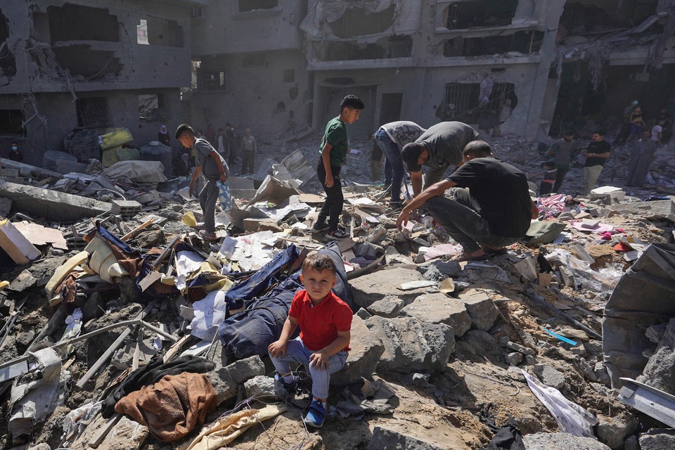 Menino palestino sentado enquanto pessoas revistam os escombros de casa destruda em ataques israelenses noturnos no campo de refugiados de al-Bureij, no centro da Faixa de Gaza (Foto: BASHAR TALEB / AFP
)