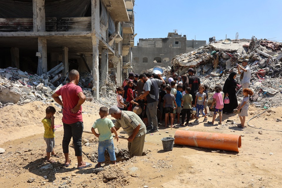 Homem escava enquanto crianas se renem em um ponto de distribuio de alimentos em meio aos escombros de edifcios destrudos durante o bombardeio israelense (Foto: OMAR AL-QATTAA / AFP
)