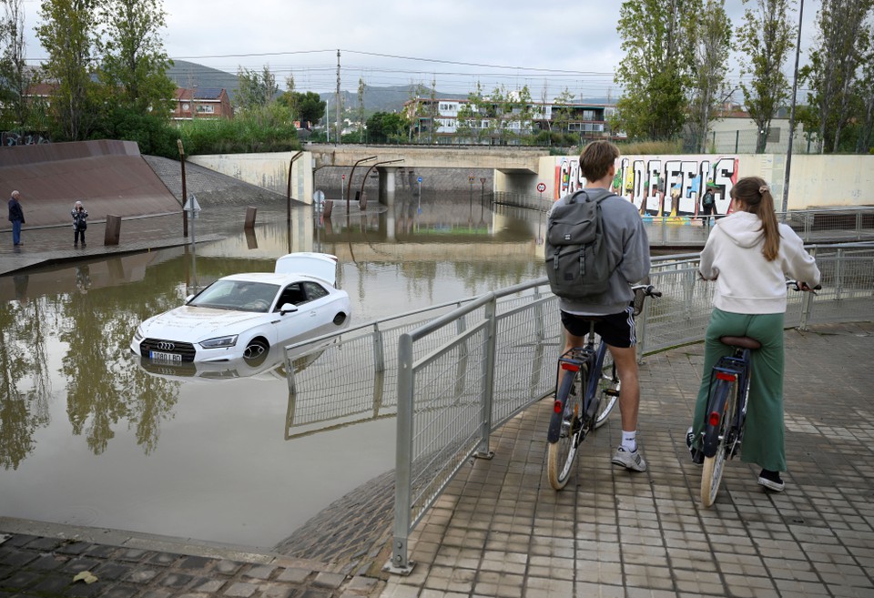 Ciclistas observam um carro inundado nos subrbios de Castelldefels, em Barcelona (Foto: Josep LAGO / AFP)